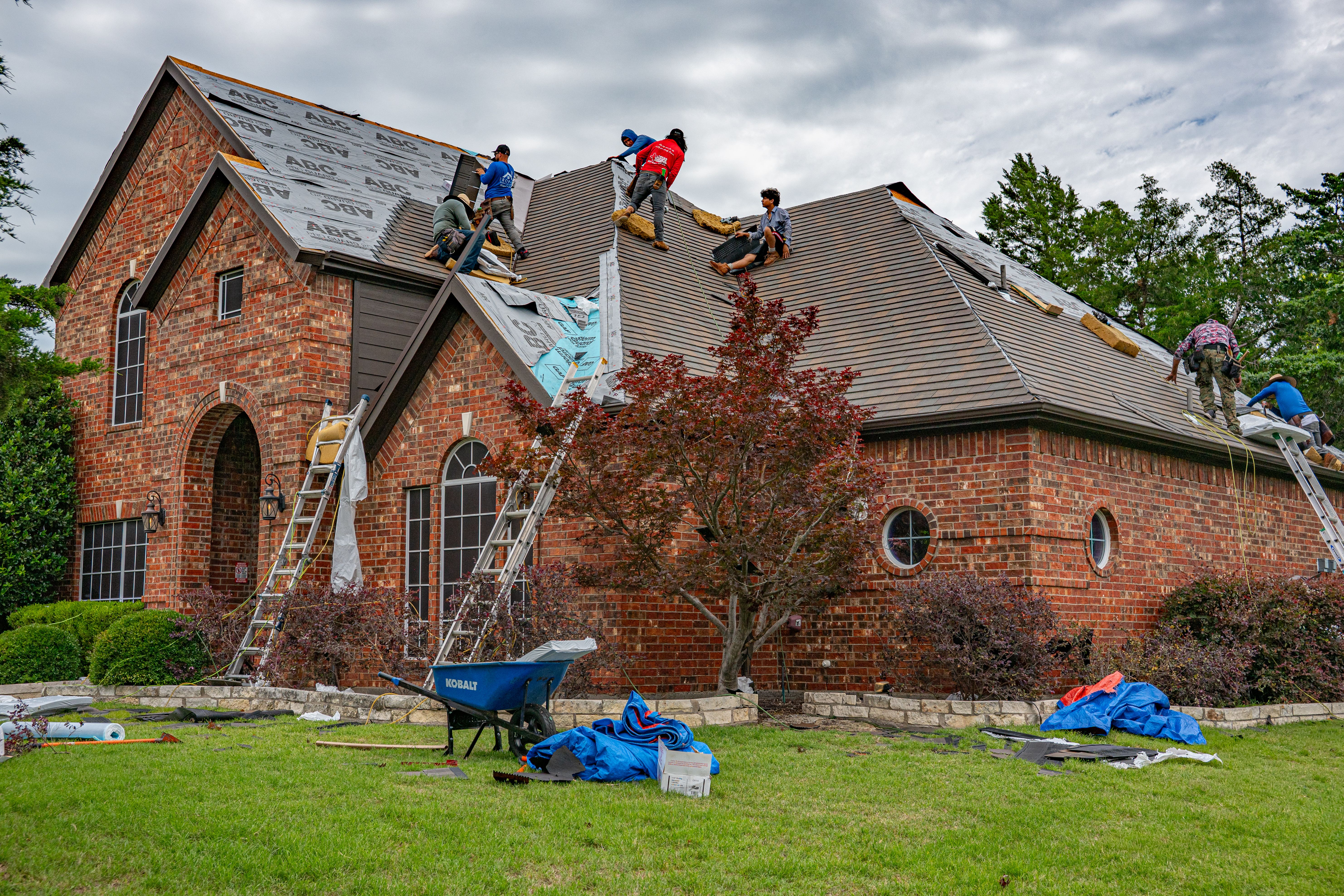 A roofer manually clearing moss from a pitched tiled roof on safe access